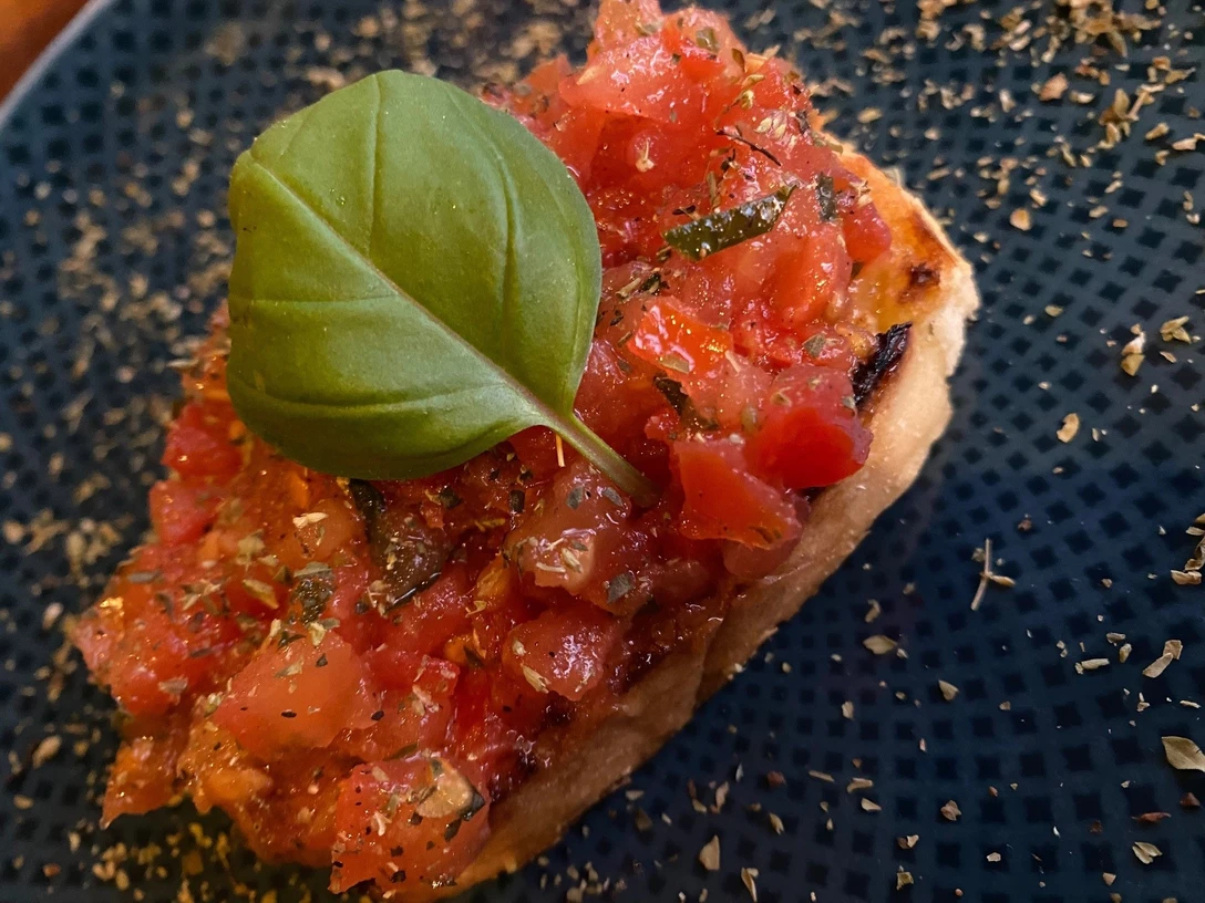 Bruschetta Frische Tomaten auf geröstetem Brot, garniert mit Basilikumblatt auf einem dunkelblauen Teller.