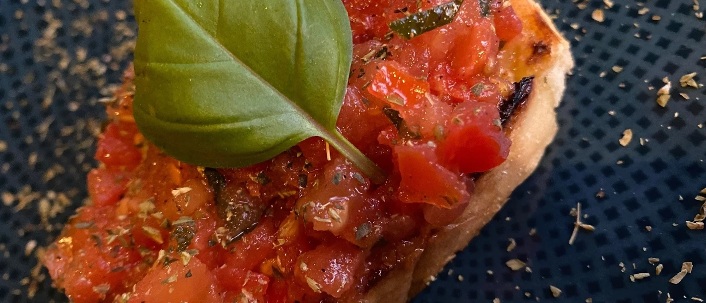 Bruschetta Frische Tomaten auf geröstetem Brot, garniert mit Basilikumblatt auf einem dunkelblauen Teller.