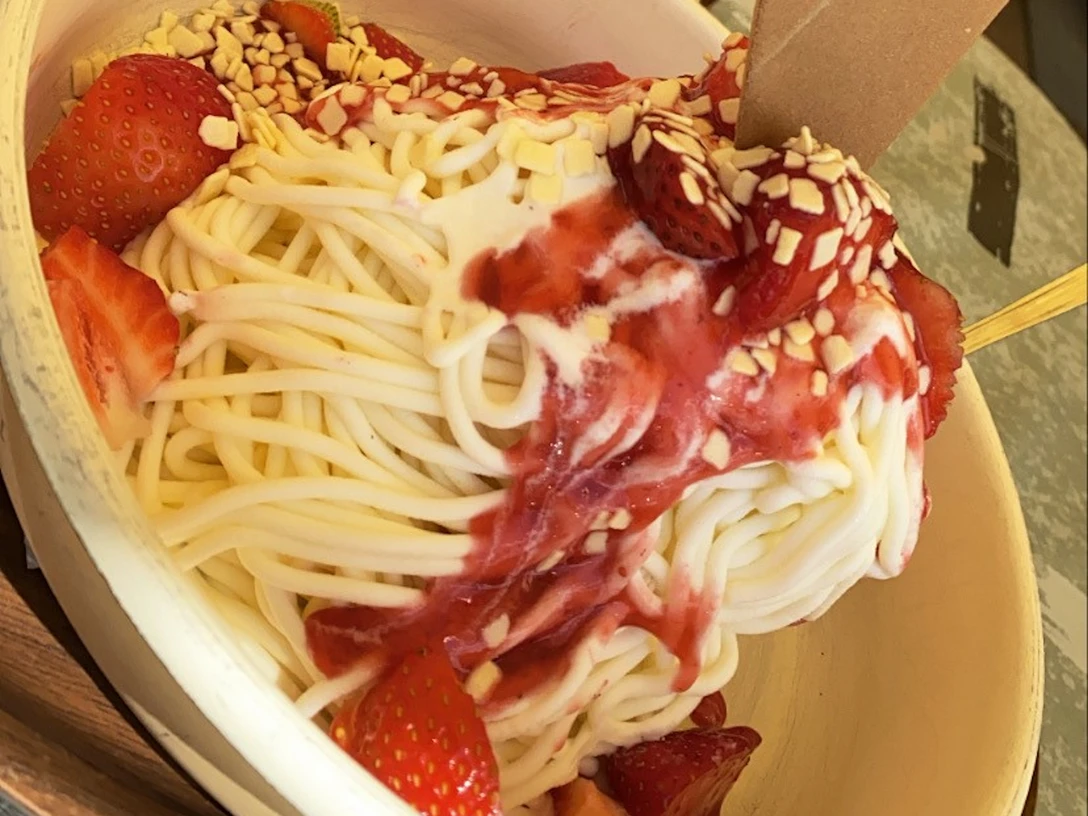 Spaghetti-Eis mit Erdbeeren, Sahne, roter Erdbeersoße und Schokoraspeln in einer weißen Schale.Spaghetti ice cream with strawberries, cream, red strawberry sauce and chocolate shavings in a white bowl.Spaghetti-is med jordbær, fløde, rød jordbærsauce og chokoladespåner i en hvid skål.Spaghetti-ijs met aardbeien, room, rode aardbeiensaus en chocoladeschaafsel in een witte kom.