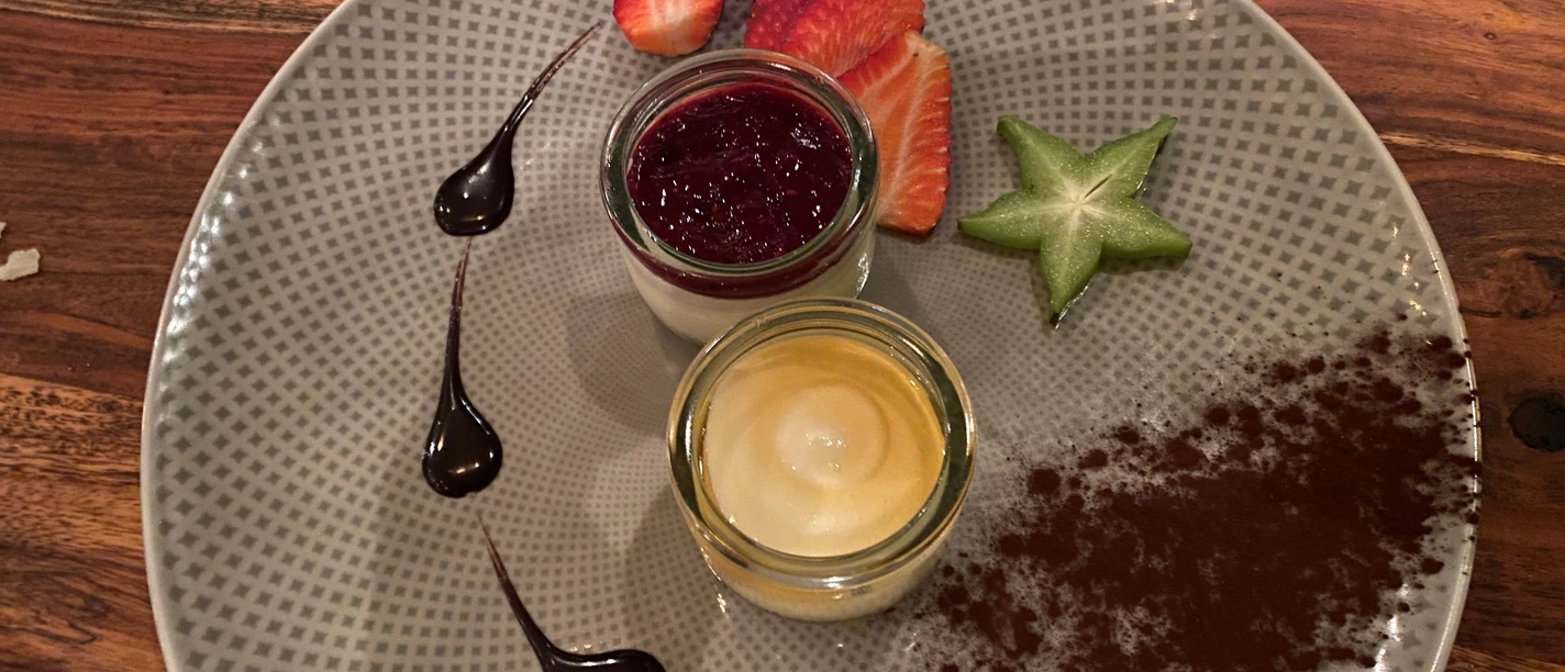 A dessert on a light-colored plate with berries, chocolate sauce and sliced star fruit.