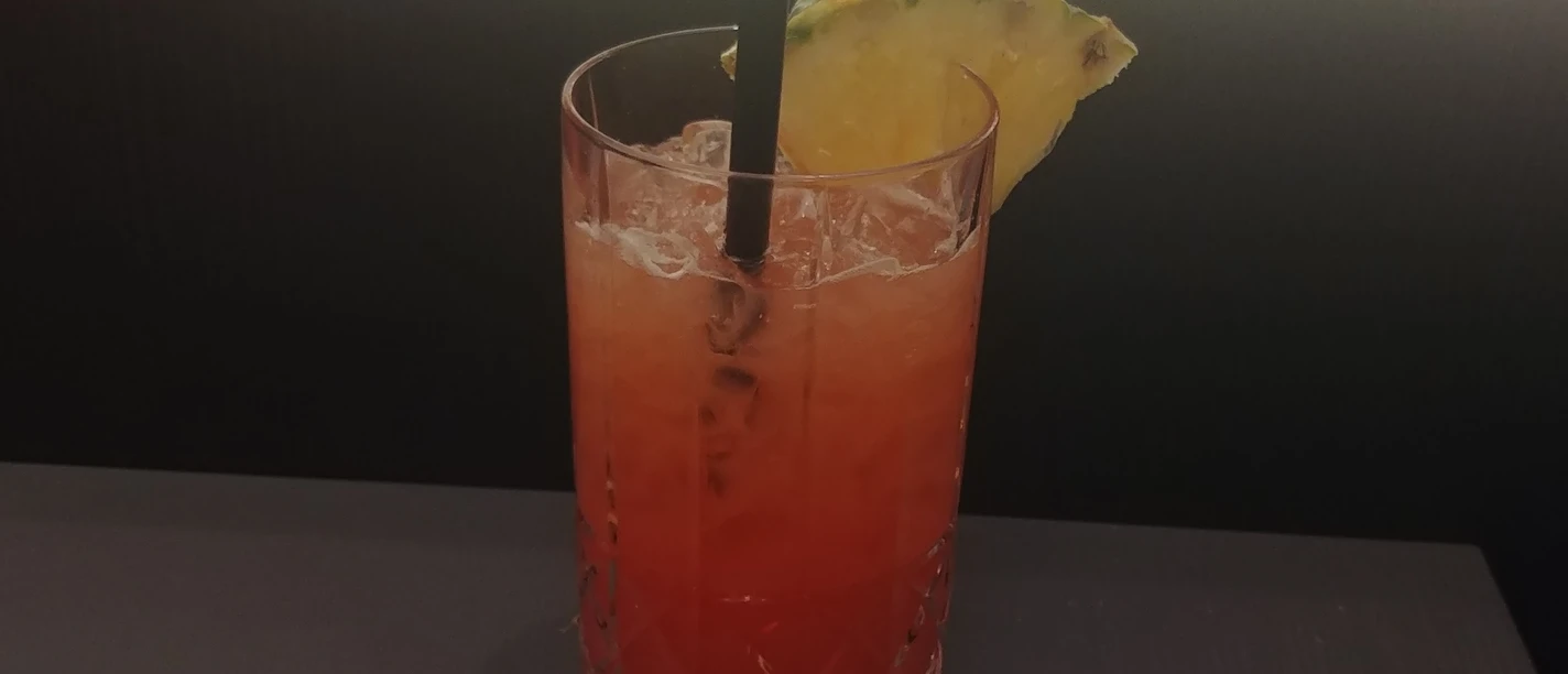 Cocktail Ein bunt geschichteter Cocktail in einem Kristallglas, dekoriert mit Ananasstück und schwarzem Strohhalm.