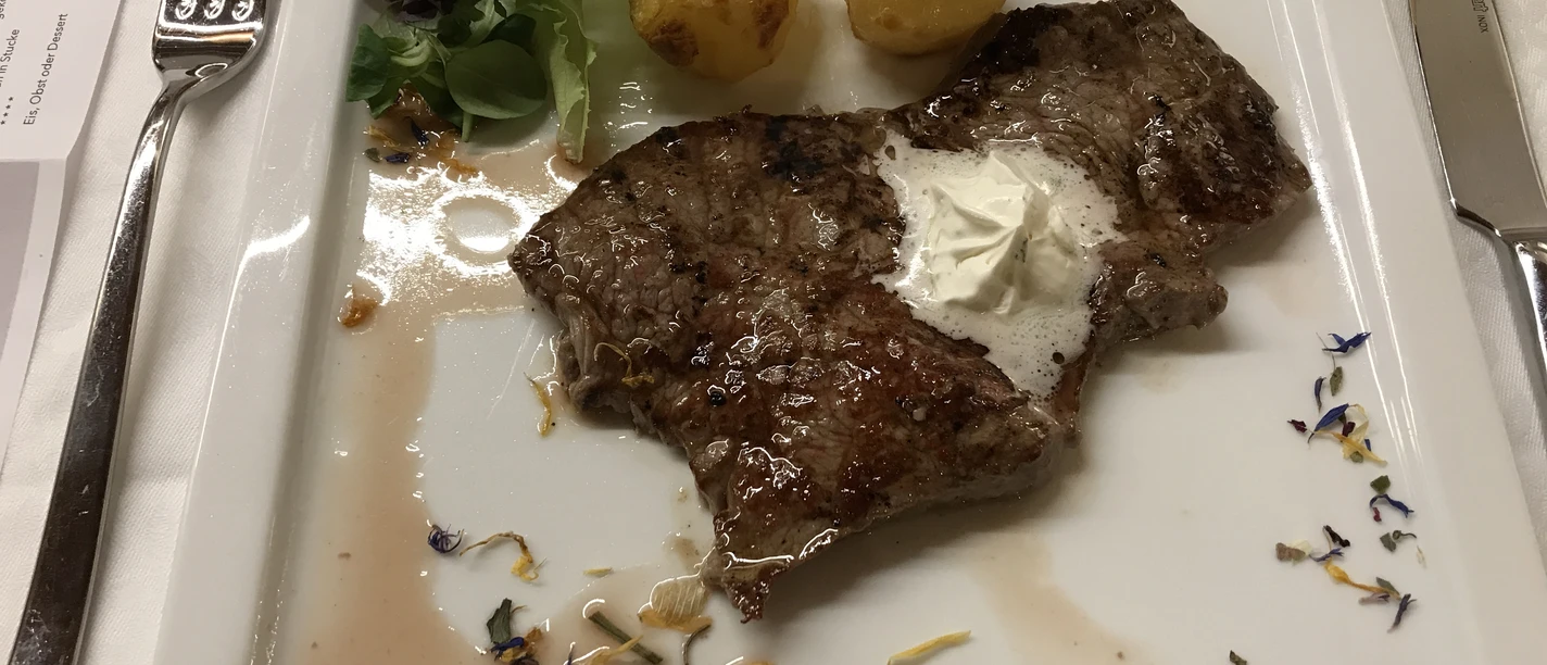 Steak Ein zartes, gegrilltes Steak auf quadratischem Teller, mit Kräuterbutter und goldenen Kartoffeln.