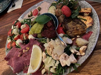 A colorful platter with various antipasti, including olives, salami, tomatoes and cheese.