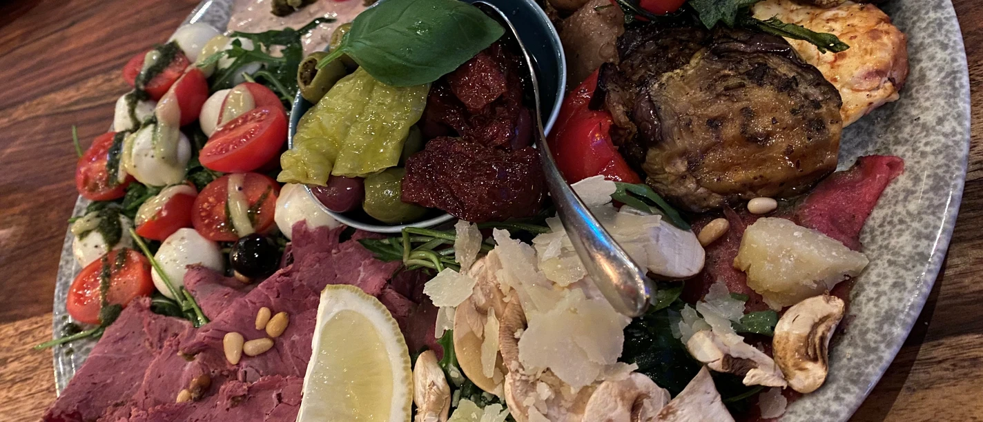 Een kleurrijke schotel met verschillende antipasti, waaronder olijven, salami, tomaten en kaas.