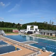freibad_hoexter (3).JPG Freibad mit großem Schwimmbecken, Sprungturm und umliegenden Gebäuden, eingebettet in grüne Landschaft.