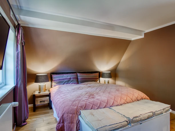 Schlafzimmer mit Doppelbett Schlafzimmer mit Doppelbett, rosa Decke und weißer Truhe unter einer braunen Dachschräge.
