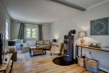 Helles Wohnzimmer mit Holzboden, schwarzem Kamin, Sofa und TV vor weißer Wand.
