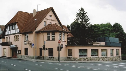 Außenansicht Historisches Gebäude mit roten Dachziegeln und Fachwerk, umgeben von Bäumen und Straße.