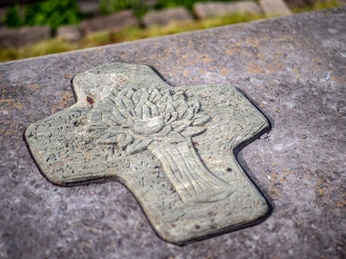 Ein Stein im Bibelgarten mit einem Kreuz drauf.