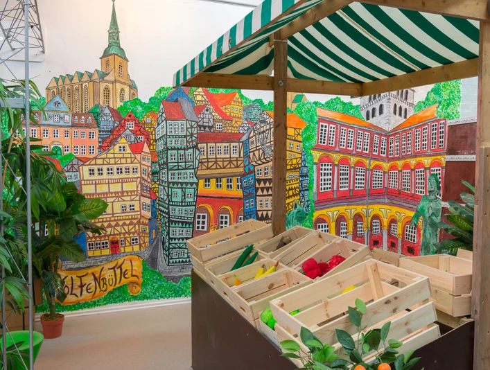 Aha_Museum-udstilling-3 Ein Marktstand. Die Wand ist bunt bemalt mit Fachwerkhäusern, dem Schloss und der HauptkircheA market stall. The wall is colorfully painted with half-timbered houses, the castle and the main churchEn markedsbod. Muren er farvestrålende malet med bindingsværkshuse, slottet og hovedkirken.Een marktkraam. De muur is kleurrijk beschilderd met vakwerkhuizen, het kasteel en de hoofdkerk