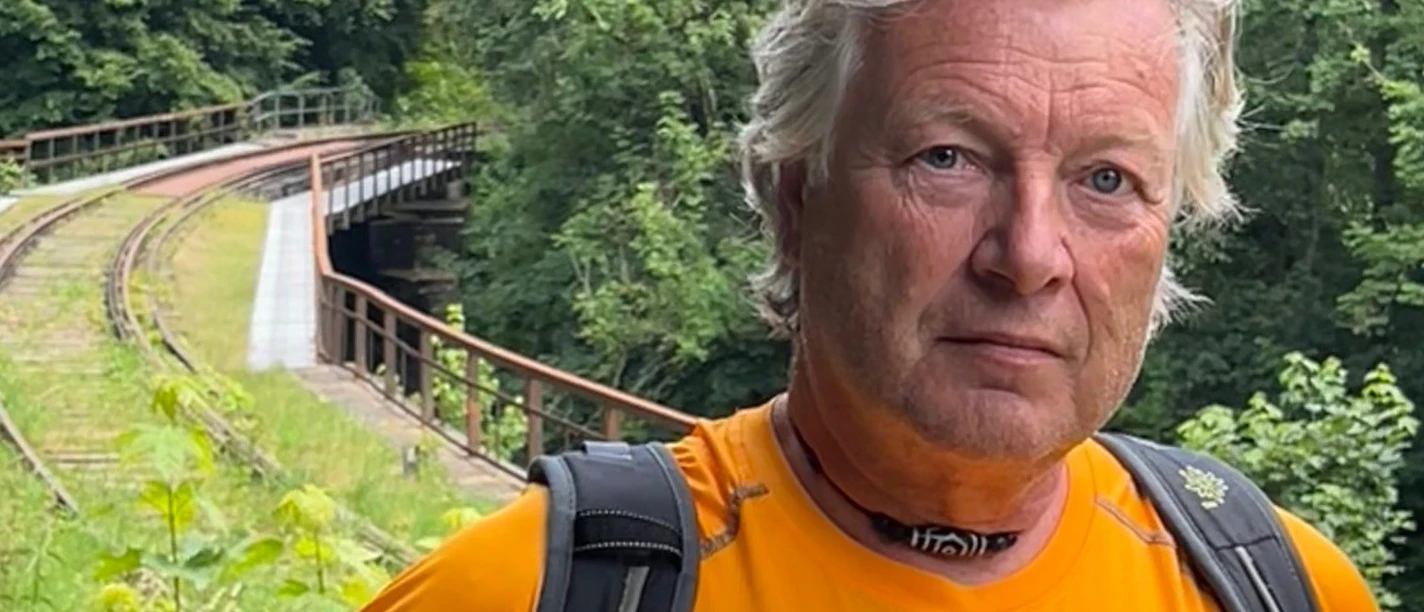 Gästeführung Michael Göbel.jpg Ein Wanderer in orangefarbenem Shirt vor einer grün bewachsenen Bahntrasse in bewaldeter Landschaft.