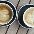 Kaffeetassen Zwei Kaffeetassen mit Latte Art in Herzform stehen auf grauen Tellern auf einem Holztisch.