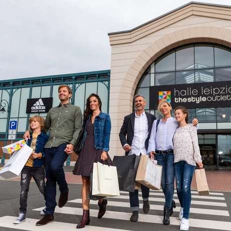 Une famille quitte le Halle Leipzig The Style Outlets Center en riant et en tenant des sacs de courses à la main, shopping, loisirs, famille, excursion
