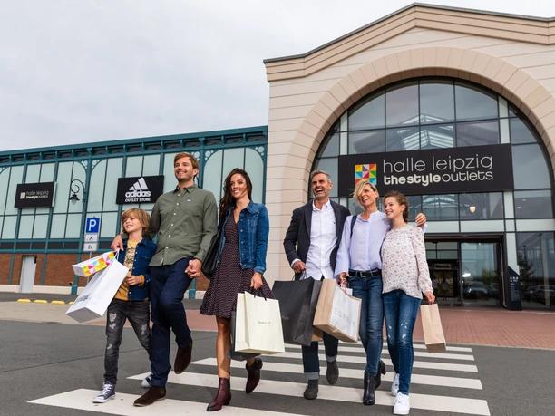 Une famille quitte le Halle Leipzig The Style Outlets Center en riant et en tenant des sacs de courses à la main, shopping, loisirs, famille, excursion