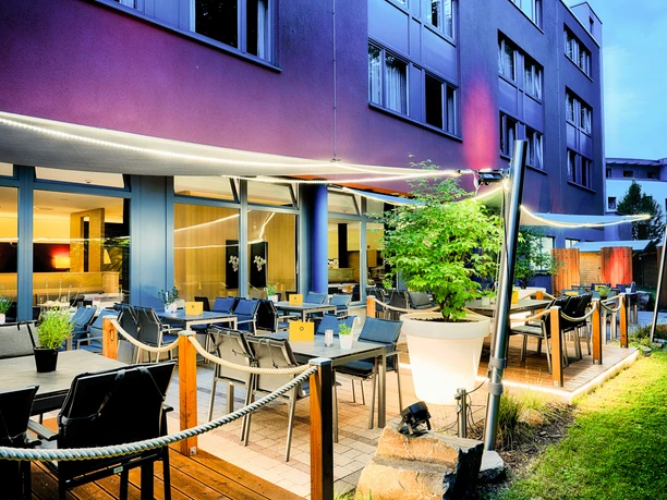 Moderne Hotelterrasse am Abend mit stimmungsvoller Beleuchtung, bequemen Sitzplätzen und Pflanzen.