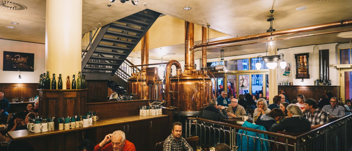 CityJazz_Turmbrauhaus_Chemnitz.jpg Eine belebte Brauhaus-Szene mit Gästen und glänzenden Kupferbiertanks im Hintergrund.