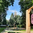 Minigolfplatz Waldkletterpark Velbert-Langenberg Ein Minigolfplatz mit Hindernis 13, umgeben von Bäumen, mit einem Turm im Hintergrund an einem sonnigen Tag.