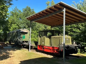 Steinhuder Meer Bahn Historische grüne Lokomotive mit überdachtem Schutz, umgeben von Wald und blauen Himmel am Steinhuder Meer.Historic green locomotive with roofed shelter, surrounded by forest and blue sky at the Steinhuder Meer.Historisk grønt lokomotiv med overdækket læskur, omgivet af skov og blå himmel ved Steinhuder Meer.Historische groene locomotief met afdak, omringd door bos en blauwe lucht aan het Steinhuder Meer.