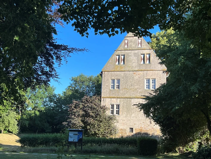 Burg Schlüsselburg Alte Burg mit steilem Dach aus hellem Stein, umgeben von Bäumen und einem blauen Himmel.