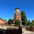 Historische Windmühle Hassel aus rotem Backstein, umgeben von Bäumen und blauen Himmel, in ländlicher Umgebung.