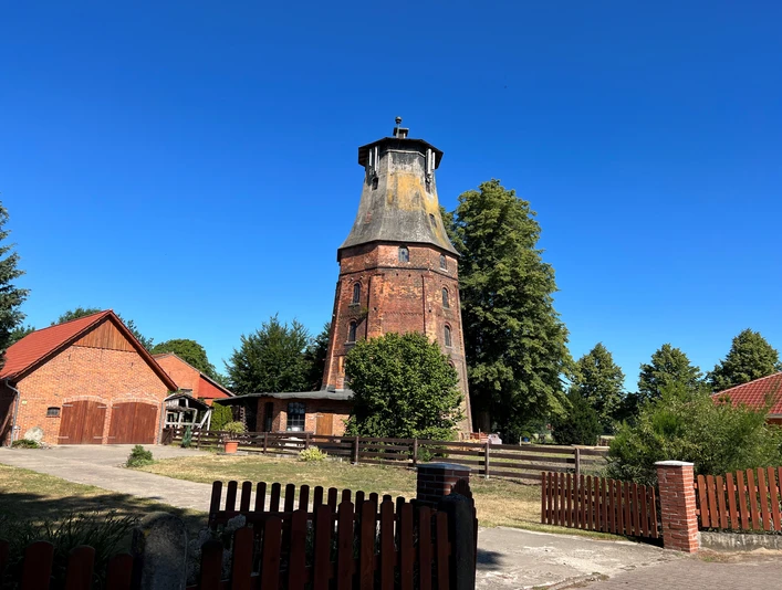 Historische Windmühle Hassel aus rotem Backstein, umgeben von Bäumen und blauen Himmel, in ländlicher Umgebung.