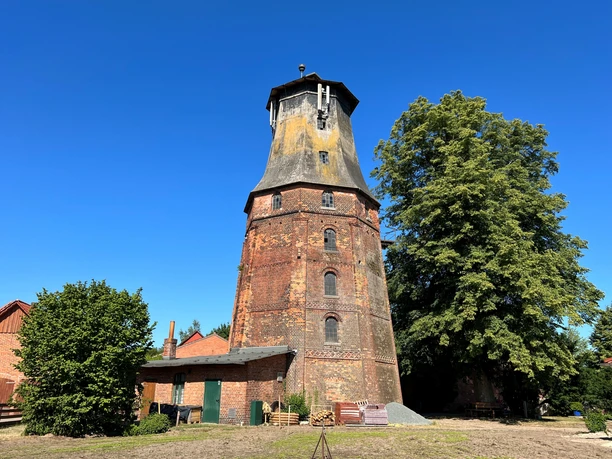 Mühle Hassel Historische Backstein-Windmühle Hassel mit schiefergedecktem Dach, umgeben von Bäumen und blauem Himmel.