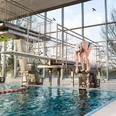 Hallenbad Angerbad in Ratingen Moderne Schwimmhalle mit Sprunganlage und großem Fenster, das viel natürliches Licht einlässt.