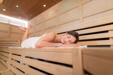 Sauna Lintorf in Ratingen Entspannende Sauna mit hölzernen Bänken, einer Person, die ruht und angenehmes Licht.