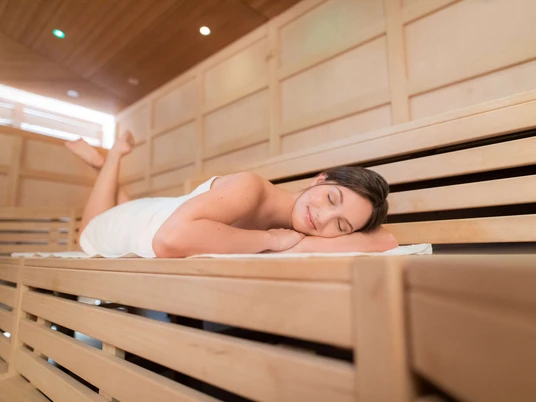Sauna Lintorf in Ratingen Entspannende Sauna mit hölzernen Bänken, einer Person, die ruht und angenehmes Licht.