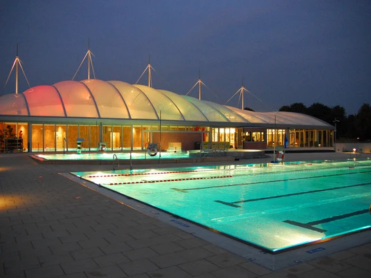Allwetterbad Lintorf in Ratingen Beleuchtetes Allwetterbad Lintorf in Ratingen, Außenansicht bei Abenddämmerung mit Pool und Pavillon.