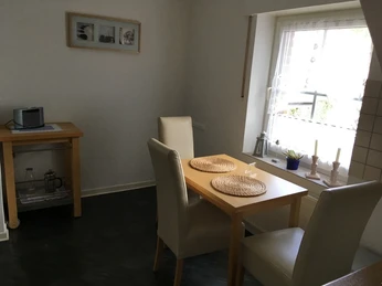 Kleines Esszimmer mit Holztisch, zwei beigen Stühlen, Fenster mit weißer Gardine, helles Ambiente.