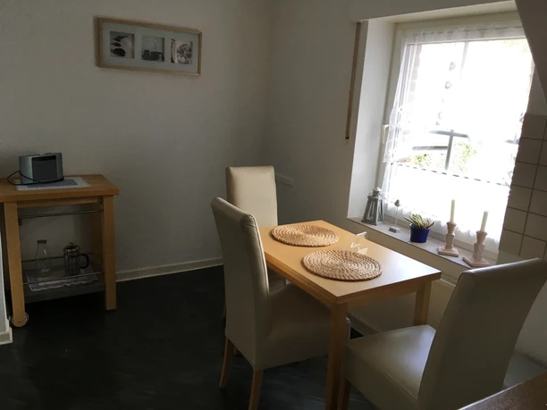 Kleines Esszimmer mit Holztisch, zwei beigen Stühlen, Fenster mit weißer Gardine, helles Ambiente.