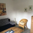 Gemütliches Wohnzimmer mit Sofa, Korbsessel und heller Holzmöbel, dekoriert mit stilvollen Bildern.