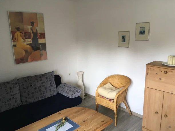 Gemütliches Wohnzimmer mit Sofa, Korbsessel und heller Holzmöbel, dekoriert mit stilvollen Bildern.