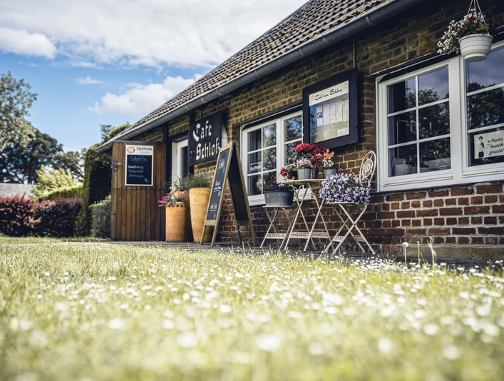 Café am Schloss, Dorsten ```html <p>Rustikales Café mit Außenbestuhlung und blühenden Pflanzen vor rot verklinkerter Fassade.</p> ```