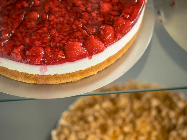 Café am Schloss, Dorsten Eine Erdbeertorte und ein Nusskuchenstück auf glänzenden Tellern in einer Kuchenvitrine.