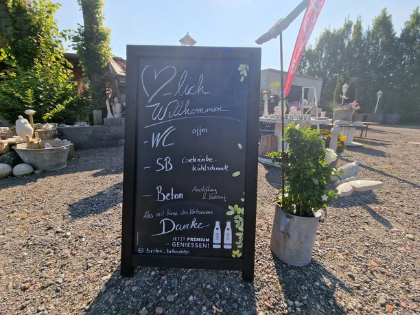 Pausenstopp in Marienheil, Rhauderfehn, Ostfriesland Schwarzes Kreidetafel-Schild mit handgeschriebener Begrüßung und Informationen zu WC, Selbstbedienung und Beton-Ausstellung im Freien