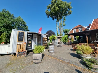 Pausenstopp in Marienheil, Rhauderfehn, Ostfriesland Kleiner Verkaufswagen mit Preislist neben einem Sitzbereich mit Tischen und Stühlen bei klarem Himmel.
