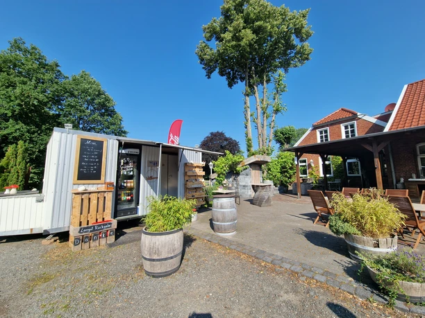 Pausenstopp in Marienheil, Rhauderfehn, Ostfriesland Kleiner Verkaufswagen mit Preislist neben einem Sitzbereich mit Tischen und Stühlen bei klarem Himmel.