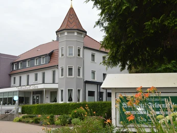 Hotel Felsenkeller mit spitzem Turm, umgeben von Bäumen und Blumen im Teutoburger Wald.