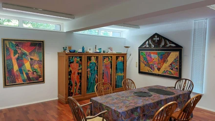 Museum Raffael Becker Ein farbenfroher Ausstellungsraum mit lebhaften Kunstwerken und einem möblierten Tisch.