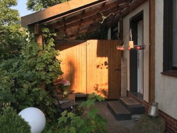 Eingangsbereich eines Hauses mit überdachtem Vordach, umgeben von viel Grün und blühenden Pflanzen.