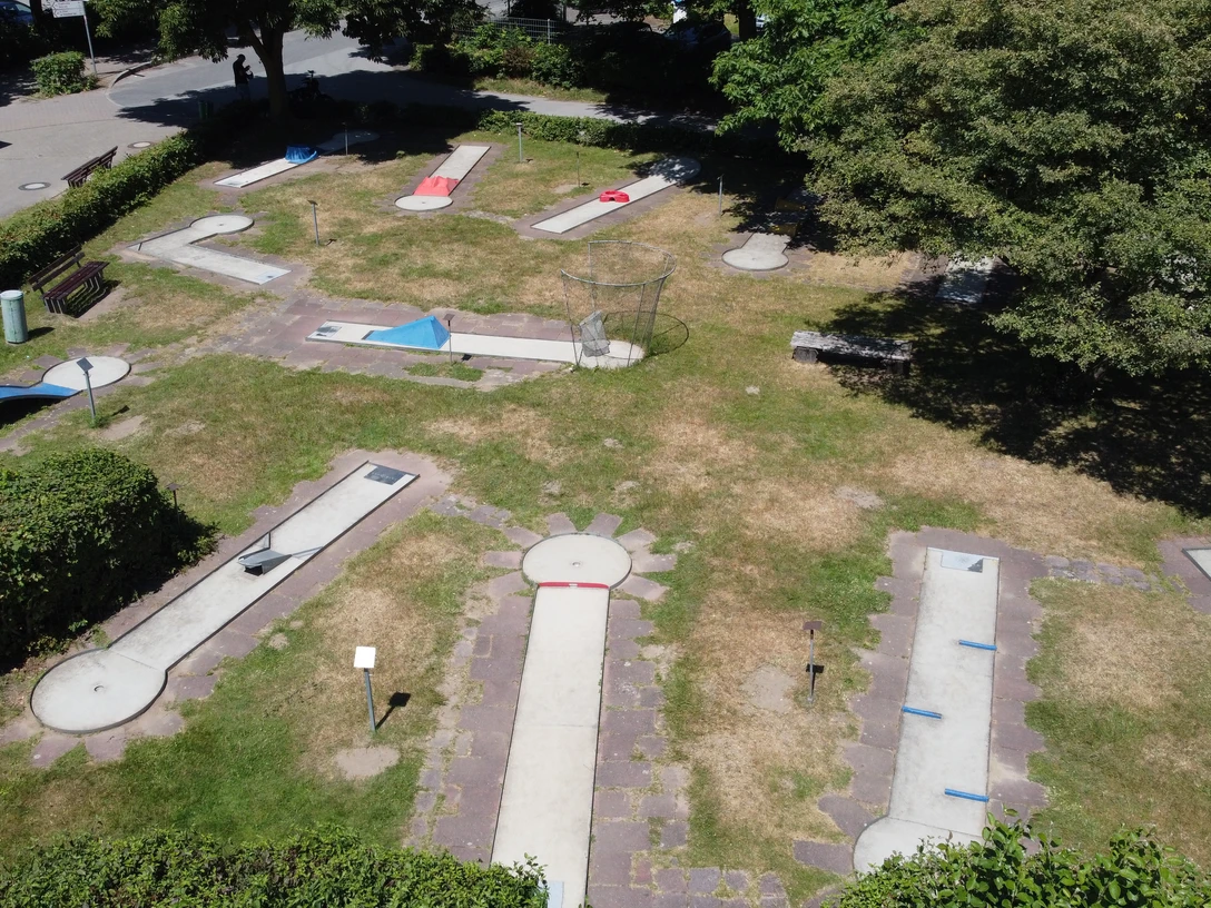 Minigolfplatz am Unterbacher See nahe Erkrath / Düsseldorf Minigolfplatz mit verschiedenen Bahnen auf einer Grünfläche, umgeben von Bäumen und Sträuchern.