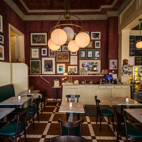 Widok na historyczną jadalnię Café Maître z meblami z kutego żelaza w stylu secesyjnym i wieloma zdjęciami na ciemnoczerwonych ścianach, kawiarnia, gastronomia, restauracja
