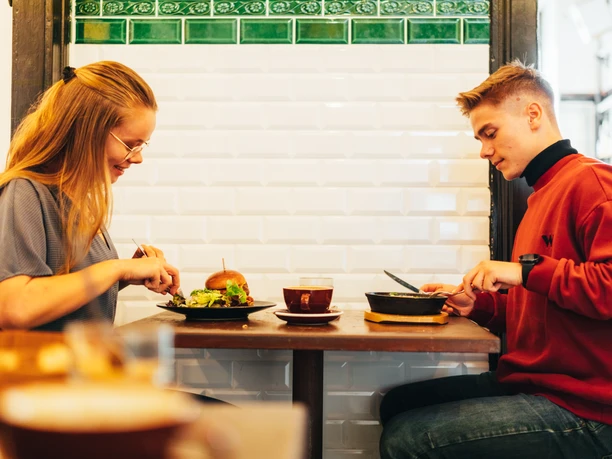 Dankbar Freisitz - Cafés à Leipzig Deux jeunes gens assis devant l'intérieur industriel de Dankbar et dégustant le menu, café, restaurant, gastronomie