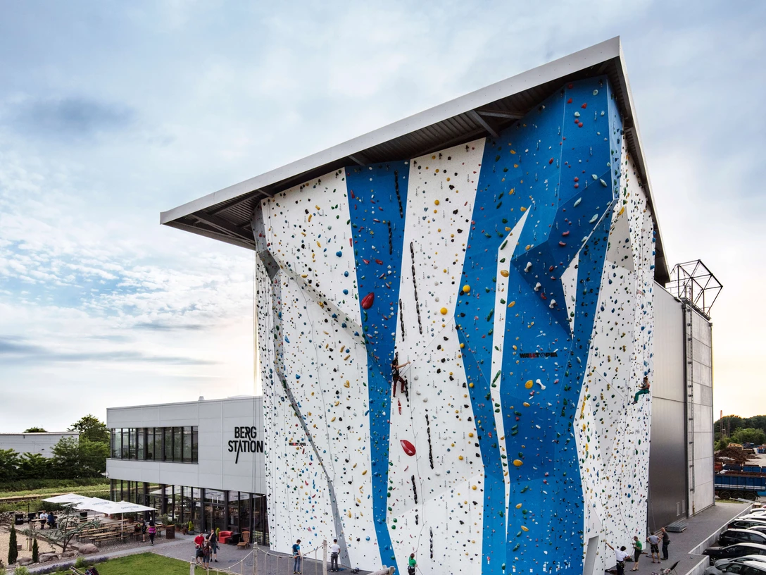 Bergstation Hilden Kletterhalle in modernem Design, großes Gebäude mit blauer und weißer Fassade, Parkplätze nahebei.