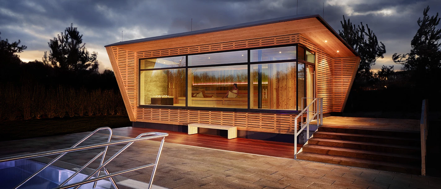 Mona Mare in Monheim am Rhein Modernes Gebäude mit großen Glasfronten, umgeben von beleuchteten Treppen und Gehwegplatten.