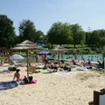 Naturfreibad Mettmann Ein Naturfreibad mit Sandstrand und Sonnenschirmen, umgeben von Bäumen und entspannenden Gästen.