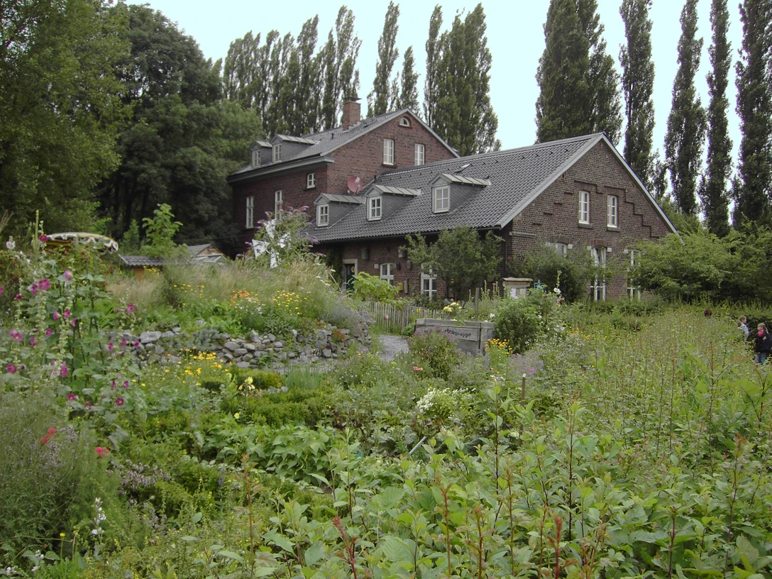 Naturschutzzentrum Bruchhausen in Erkrath Ein historisches Backsteingebäude umgeben von einer üppigen, vielfältigen Gartenlandschaft im Naturschutzgebiet.