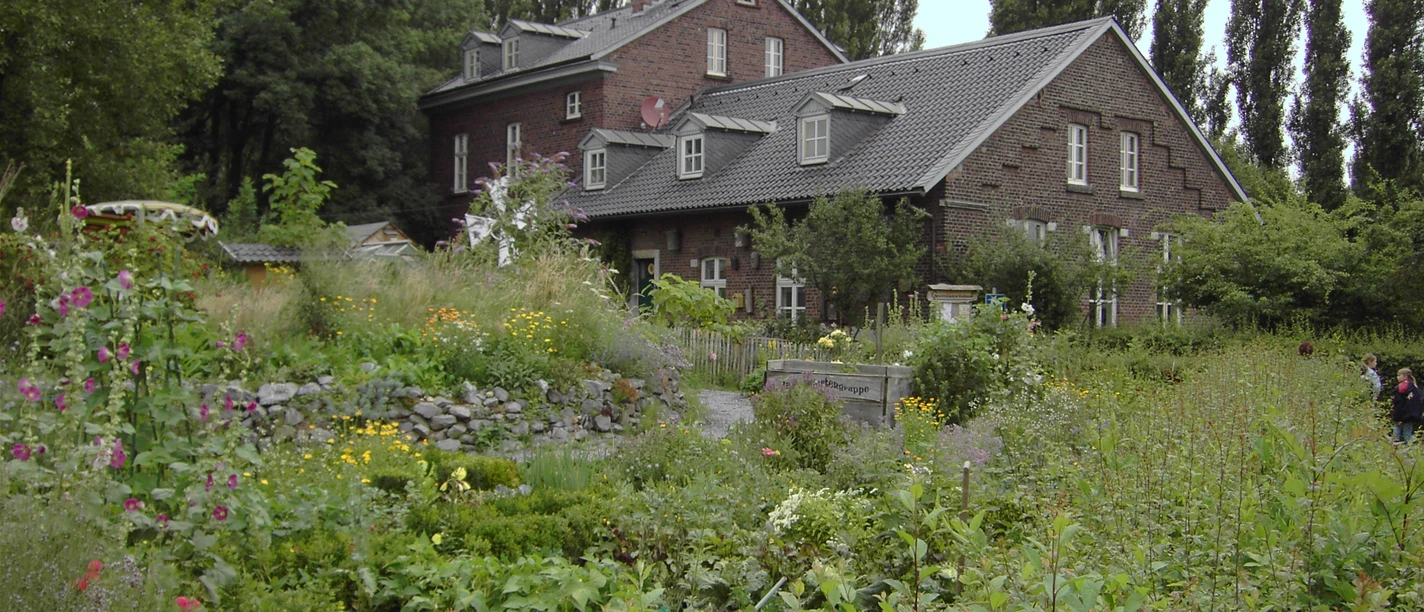 Naturschutzzentrum Bruchhausen in Erkrath Ein historisches Backsteingebäude umgeben von einer üppigen, vielfältigen Gartenlandschaft im Naturschutzgebiet.